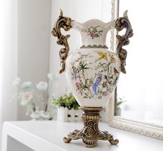 an ornate vase sitting on top of a white table next to a mirror and flowers