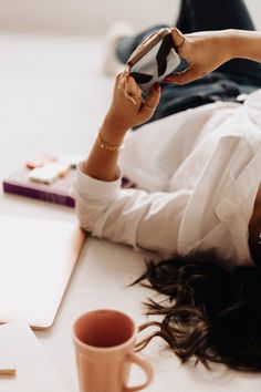 a woman laying on the floor with her cell phone and coffee cup in front of her