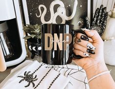 a woman holding a black coffee mug with the word dnd on it in gold lettering