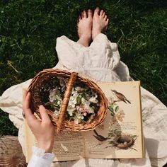 a person laying on the grass reading a book and holding a basket with flowers in it