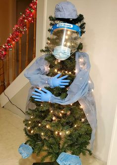 a mannequin dressed in blue gloves and protective gear stands next to a christmas tree