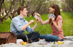 a man and woman sitting on the grass playing cards with each other in their hands