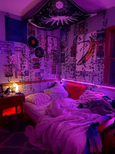 an unmade bed in a room with purple lighting and pictures on the wall behind it