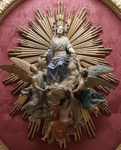 a statue of the virgin mary surrounded by angels in a gold frame on a red wall