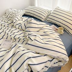 an unmade bed with blue and white striped comforter, pillows and coffee cup