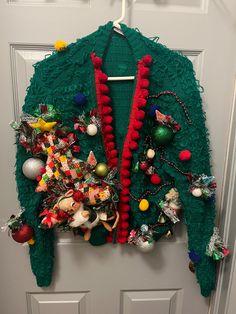 a green sweater with red trim and ornaments hanging from it's side on a door