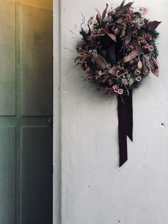 a wreath hanging on the side of a white wall next to a door with a black ribbon