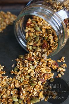 granola in a glass jar on top of a baking sheet with nuts scattered around it