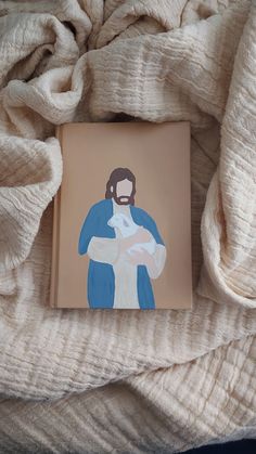 a book with a painting of jesus holding a baby in it's arms on top of a blanket