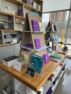 a table with books on it in front of a window and shelves full of books