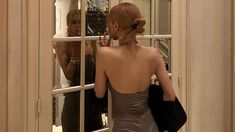 a woman standing in front of a window looking into the mirror with her back to the camera