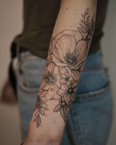 a woman's arm with flowers on it and a black ink tattoo that is in the shape of a flower