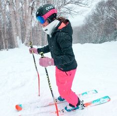 a woman in pink pants and black jacket on skis with trees in the background