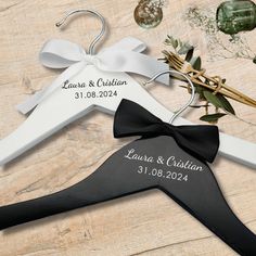 two personalized wedding hangers with a black and white bow on them, next to a bouquet of flowers