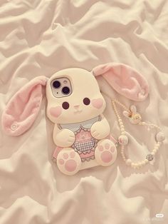 an iphone case with a bunny holding a beaded necklace on top of a bed