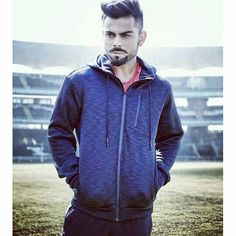 a man standing in front of a stadium wearing a blue hoodie and black sweatpants