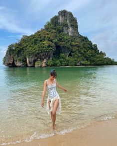 a woman in a white dress walking out of the water on a beach near an island