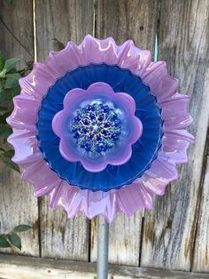 a blue and purple flower sitting on top of a metal pole next to a wooden fence