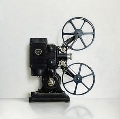 an old fashioned movie projector sitting on top of a white table next to a wall