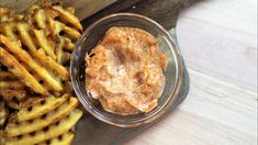 a wooden cutting board topped with french fries and a bowl of dipping sauce next to it