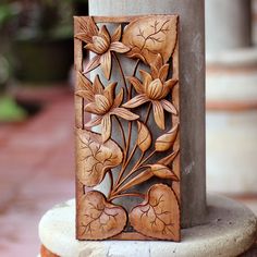 an intricately carved wooden object on top of a stone pillar with flowers and leaves