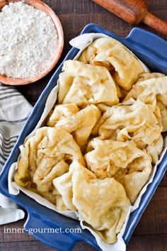 some dumplings are in a blue dish next to a bowl of flour and a wooden spoon