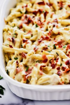 a white casserole dish filled with pasta and bacon, garnished with parsley