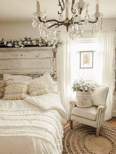 a white bed sitting in a bedroom next to a window with a chandelier