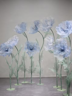 blue flowers are arranged in glass vases on the floor next to a white wall