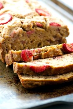 sliced bread with strawberries on it sitting on a table next to another loaf of bread