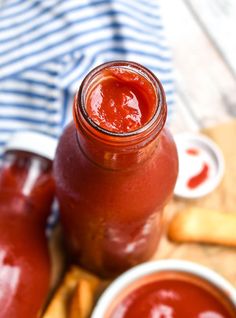 a jar filled with ketchup sitting next to some french fries on a table