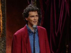 a man standing in front of a microphone and wearing a red jacket on top of a stage