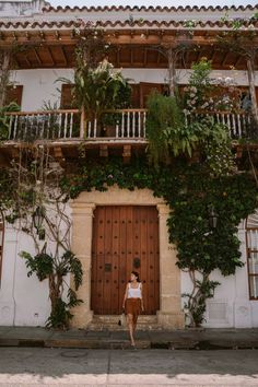 a woman standing in front of a building with vines growing on the side of it