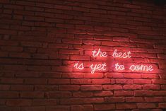 a brick wall with a neon sign that says, the best is yet to come