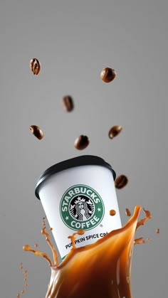 a cup of starbucks coffee is being poured into the ground with some coffee beans coming out of it