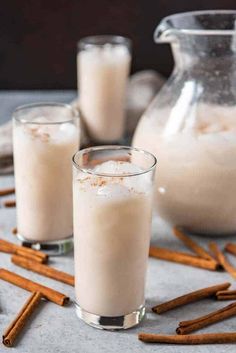 two glasses filled with ice cream and cinnamon sticks on a table next to a pitcher