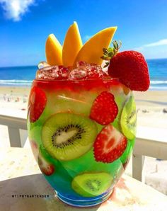 a glass filled with fruit on top of a table next to the ocean and beach