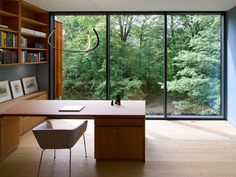 an office with a desk, bookshelf and large window overlooking the trees outside