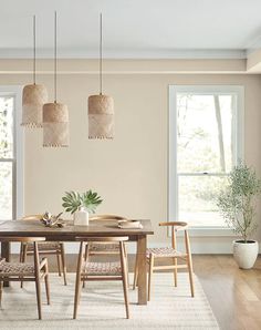 a dining room table and chairs in front of two large windows with wooden flooring