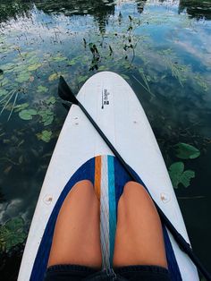 the person is paddling their kayak on the water with lily pads and oars