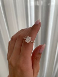 a woman's hand holding a diamond ring in front of a white background with curtains