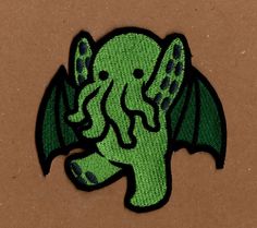 an embroidered green elephant head with black eyes and tail, sitting on a brown surface