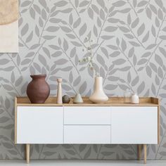 a table with vases on it in front of a wallpapered background that looks like leaves