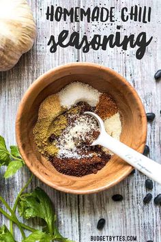 the ingredients for homemade chili seasoning in a wooden bowl next to garlic and pepper