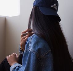 a woman with long hair wearing a blue hat and denim jacket sitting on the floor