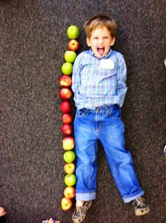 a little boy laying on the ground next to some apples and an apple tower with his mouth open