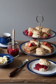 three plates with pastries and jam on them sitting on a wooden table next to cups