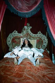 a woman is laying in bed with an elaborate headboard and red drapes around her