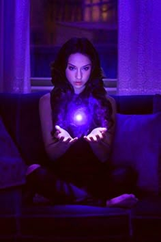 a woman sitting on a couch holding a glowing ball in her hands