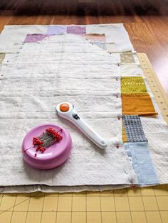 a piece of fabric and a pink plate on a table with a sewing needle next to it